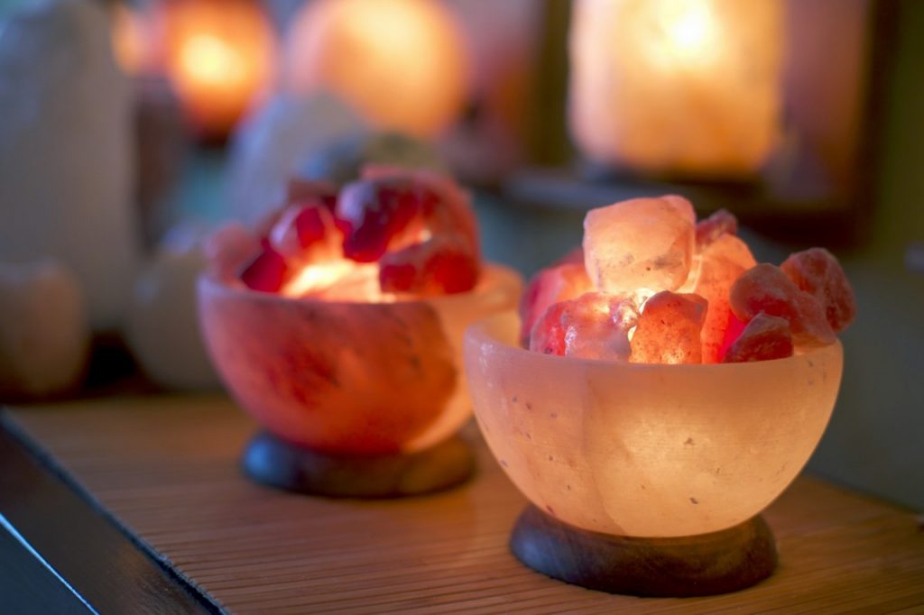 Bowls of pink salt lit from within, glowing on a wooden shelf