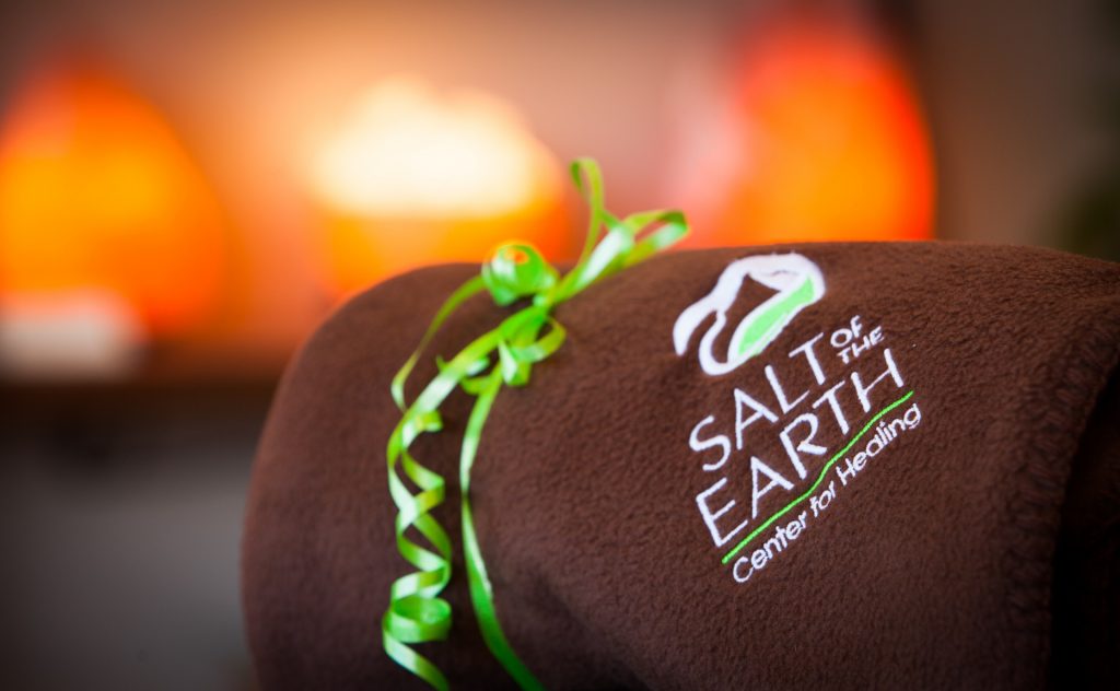 A rolled Salt of the Earth blanket wrapped in a green ribbon with salt lamps visible behind